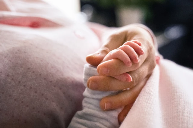 Newborn baby hand gripping parent finger on pink blanket representing birth injury legal advocacy