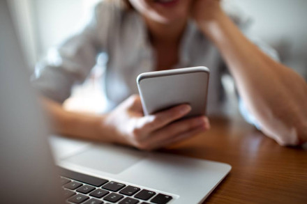Woman checking smartphone while working at laptop desk representing business communication and case research