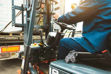 Forklift operator in blue uniform maneuvering equipment at industrial loading dock