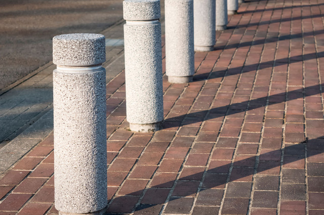 Row of concrete security bollards lining brick pedestrian walkway to prevent vehicle intrusion on property