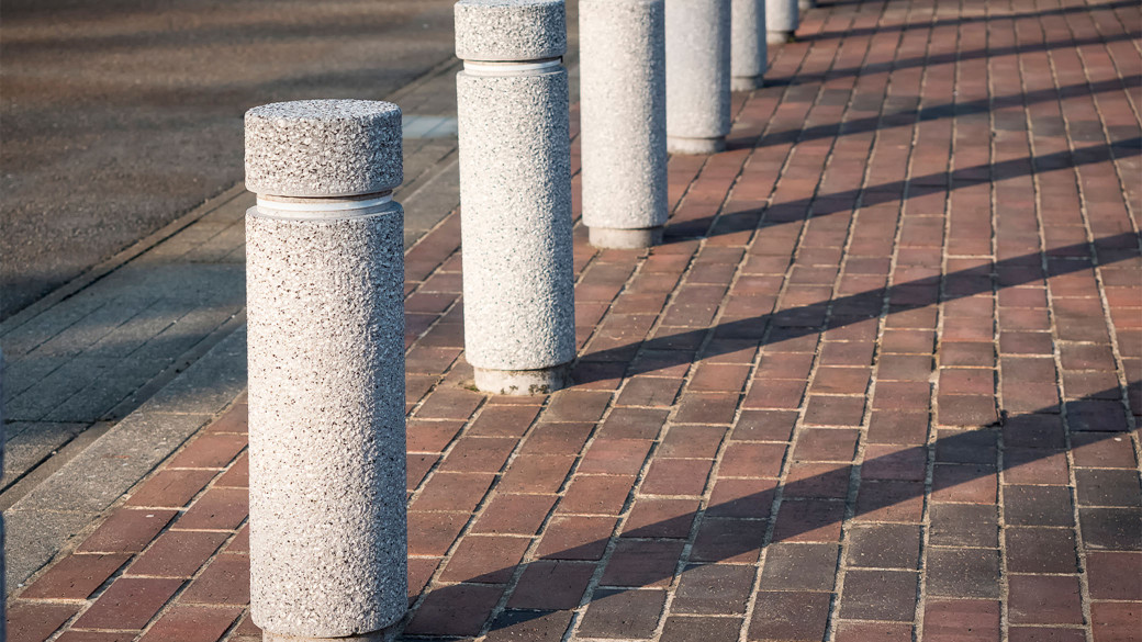 Row of concrete security bollards lining brick pedestrian walkway to prevent vehicle intrusion on property