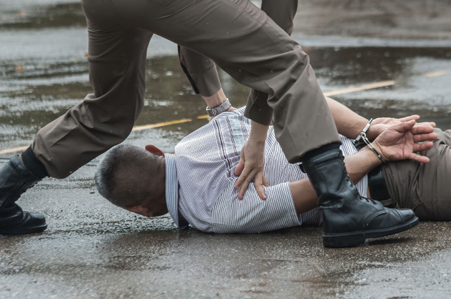 Uniformed officer pinning a handcuffed man face-down on wet pavement, representing ICE enforcement abuse and excessive force claims