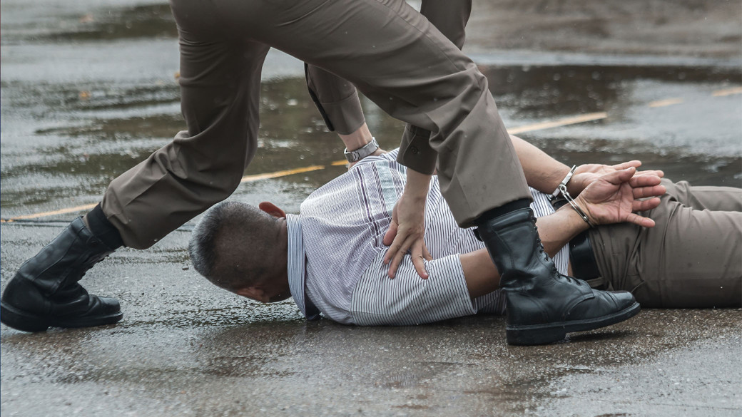 Uniformed officer pinning a handcuffed man face-down on wet pavement, representing ICE enforcement abuse and excessive force claims