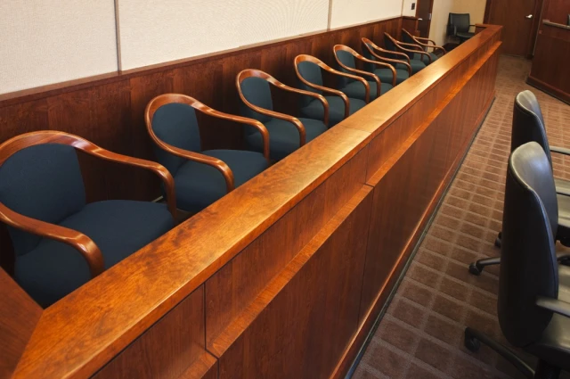 Empty jury box with navy upholstered chairs along polished wood railing in modern criminal defense courtroom