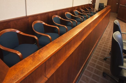 Empty jury box with navy upholstered chairs along polished wood railing in modern criminal defense courtroom