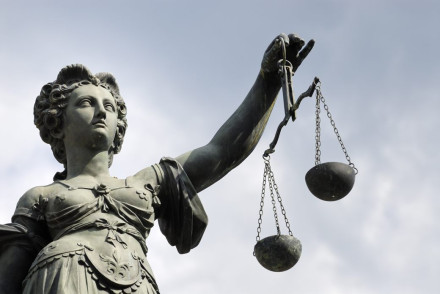 Lady Justice bronze statue holding scales aloft against overcast sky representing impartial criminal defense law