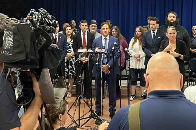 Attorney addressing media at press conference with clients and legal team standing in support