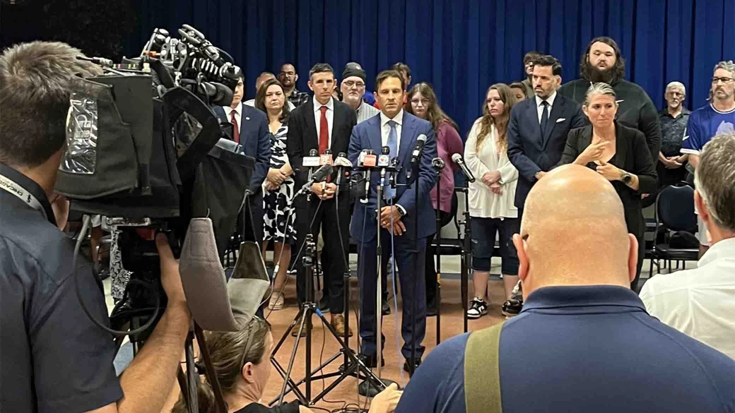 Attorney addressing media at press conference with clients and legal team standing in support