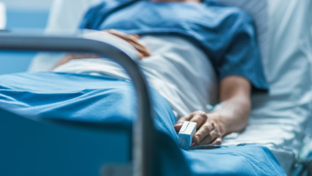 Hospital patient in gown with pulse oximeter lying in bed during medical injury recovery