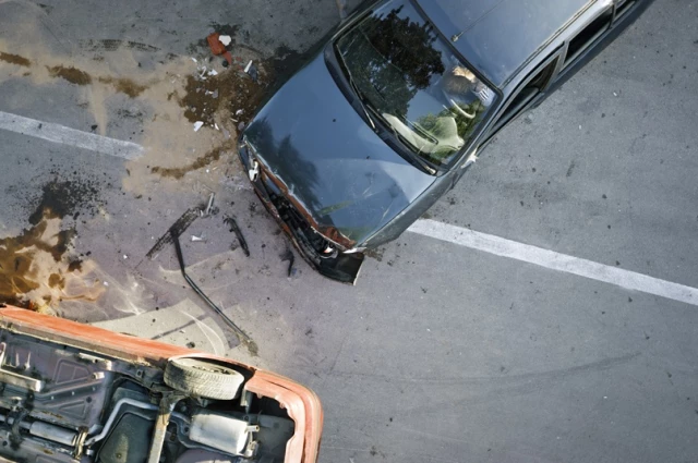 Aerial view of two vehicles after a collision, one overturned with fluid and debris on the roadway