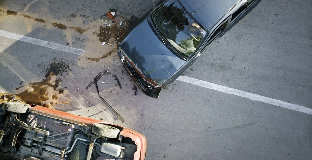 Aerial view of two vehicles after a collision, one overturned with fluid and debris on the roadway