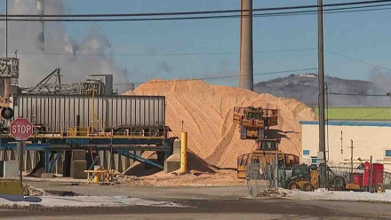 Industrial paper mill in Rumford Maine with wood chip pile and heavy equipment in winter