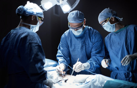 Three surgeons in blue gowns operating under bright lights representing surgical negligence and malpractice claims