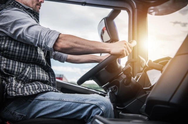 Truck driver in plaid shirt gripping steering wheel inside commercial vehicle at sunset