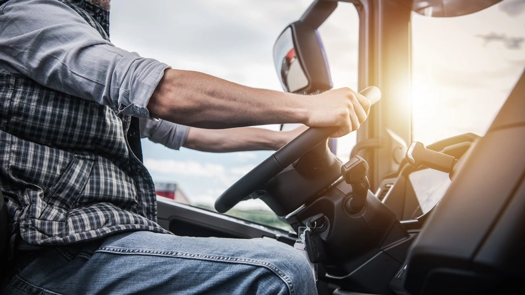 Truck driver in plaid shirt gripping steering wheel inside commercial vehicle at sunset