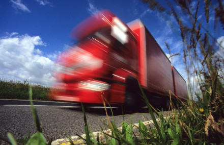 Red semi-truck speeding past low camera angle with motion blur conveying dangerous truck speed